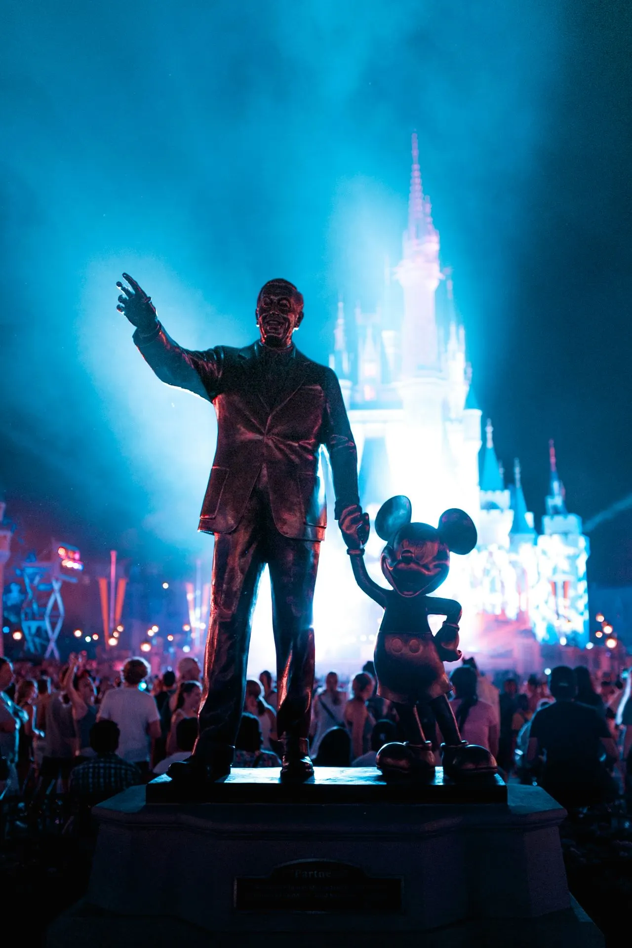 Theme park castle lit up at night behind a statue