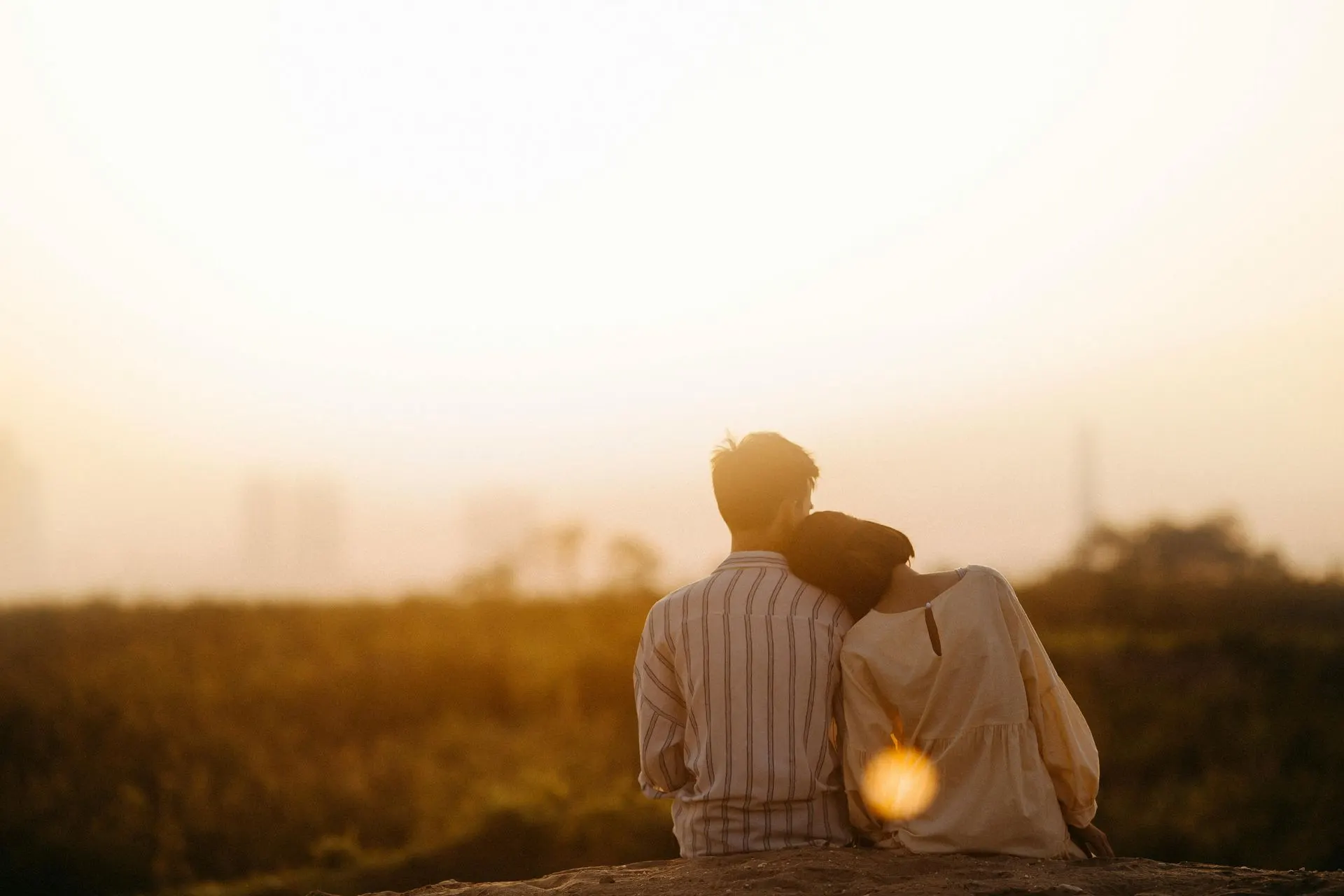 Couple sitting close together in a field at sunset