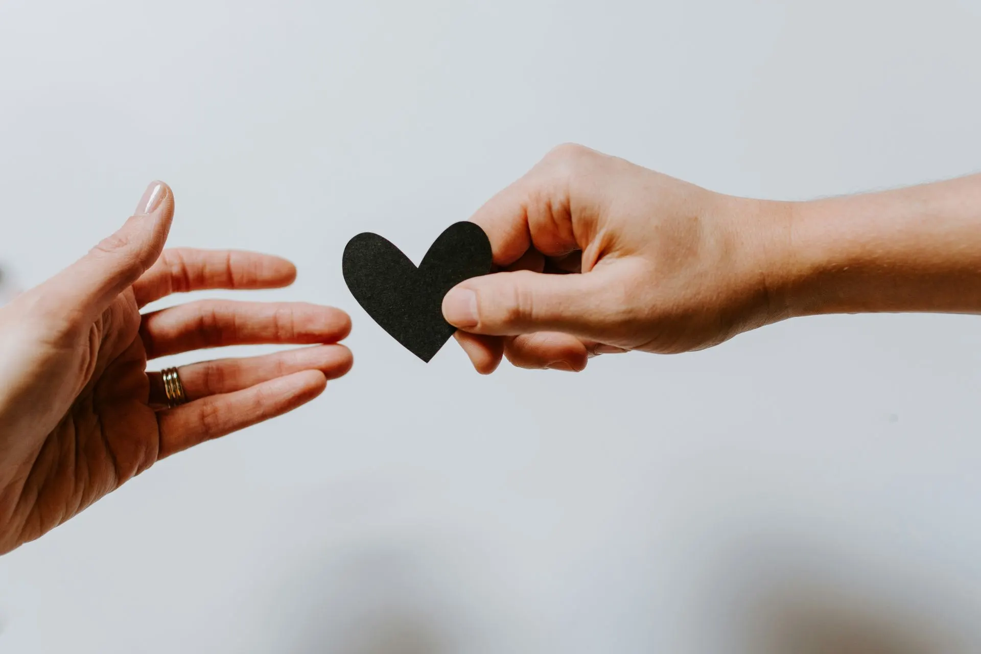 Two hands passing a small black paper heart